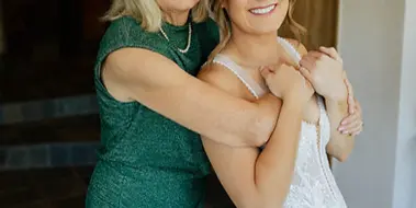 A smiling bride with styled hair and makeup posing with an older woman in a green dress.
