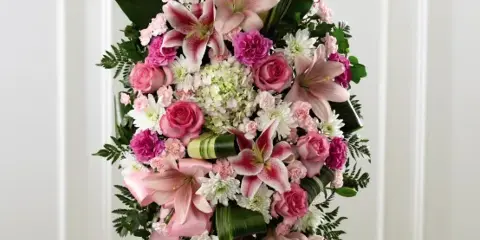 A tall floral standing spray featuring pink lilies, roses, and carnations on a white stand.