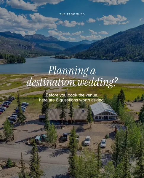 Aerial view of a rustic wedding venue building situated on the shore of a large lake with mountains in the background.