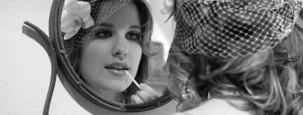 Bride applying lip makeup while looking into a mirror with a floral headpiece