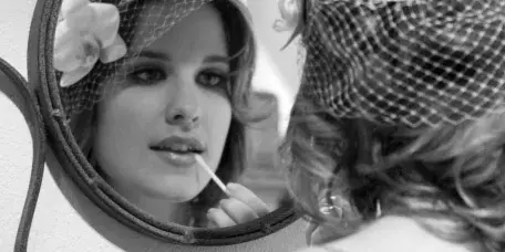 Bride applying lip makeup while looking into a mirror with a floral headpiece