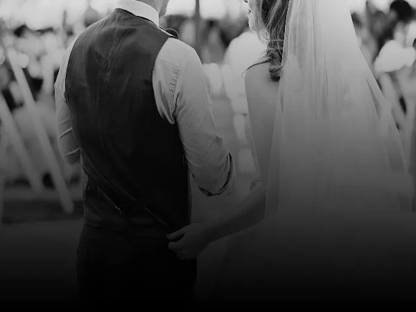 A black and white photograph of a bride and groom standing together at a wedding ceremony.