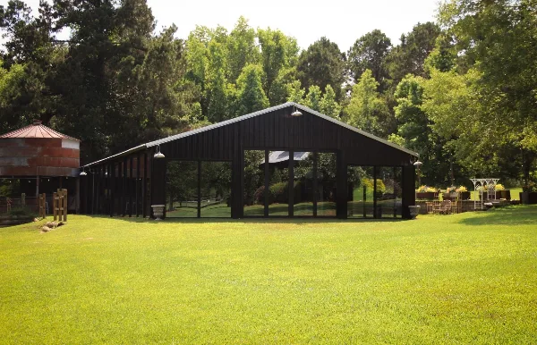 Open-sided dark wood event pavilion on a grassy lawn with a water tower and trees in the background.
