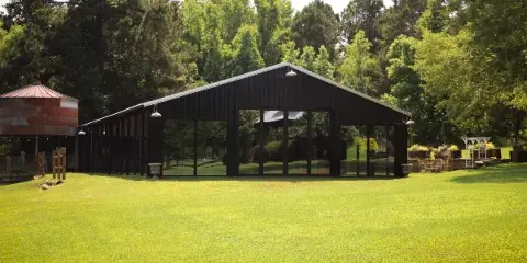 Open-sided dark wood event pavilion on a grassy lawn with a water tower and trees in the background.