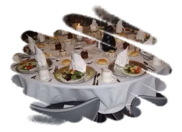 A round catering table set with white linens, folded napkins, plates of salad and rolls, and formal place settings.