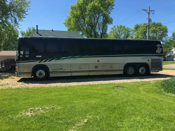 A black and silver party bus with green graphics parked on a gravel driveway in front of a grassy area.