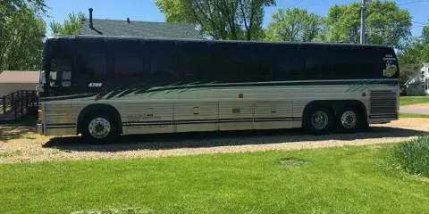 A black and silver party bus with green graphics parked on a gravel driveway in front of a grassy area.