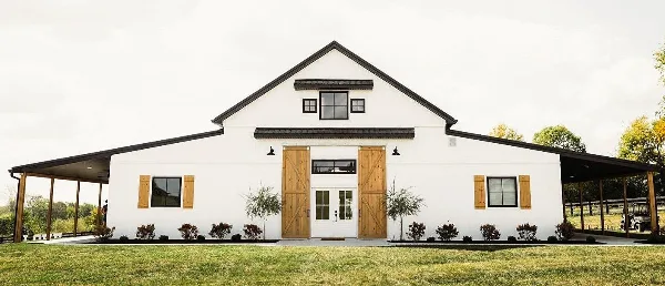 Exterior view of a white barn wedding venue with wooden doors and black trim.