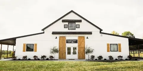 Exterior view of a white barn wedding venue with wooden doors and black trim.