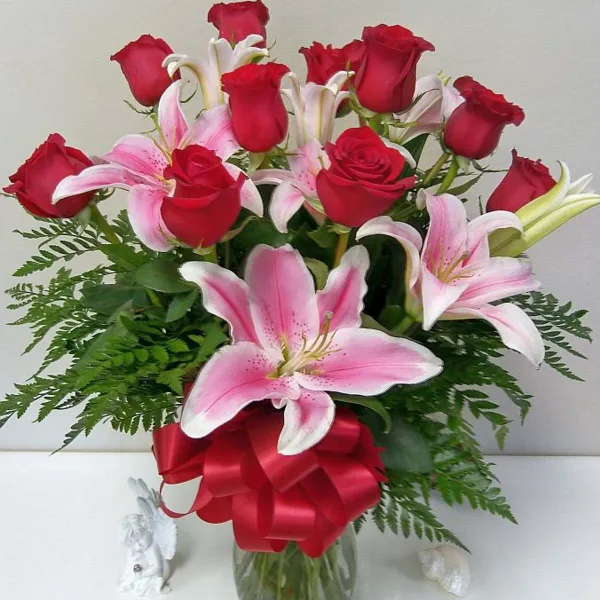 A floral arrangement of red roses and pink lilies in a glass vase with a red ribbon.
