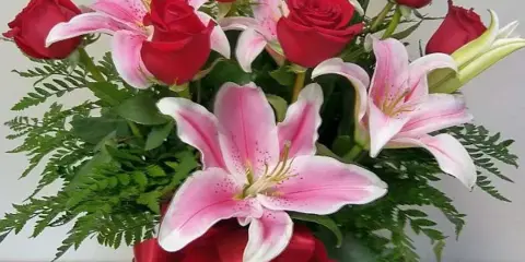 A floral arrangement of red roses and pink lilies in a glass vase with a red ribbon.