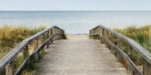 A wooden boardwalk pathway leading through dune grass to a sandy beach and the ocean.