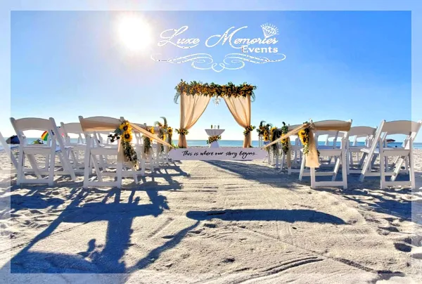 A beach wedding ceremony setup featuring a floral arch, draped fabric, and rows of white chairs.
