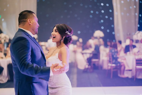 A bride and groom dancing at a wedding reception with guests seated in the background.