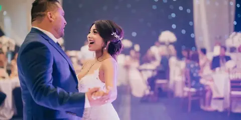 A bride and groom dancing at a wedding reception with guests seated in the background.
