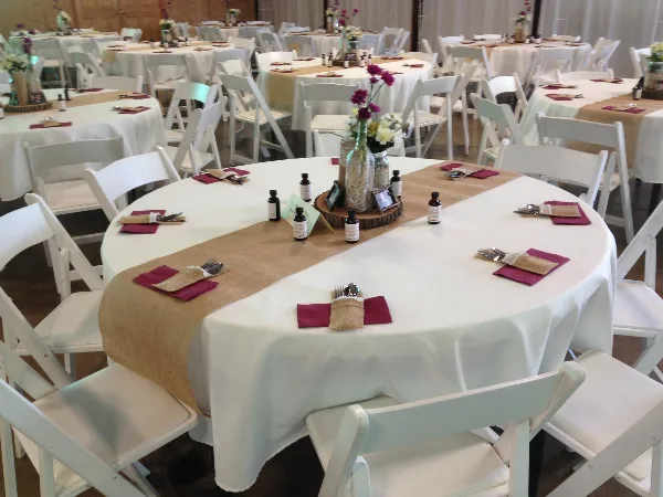 Interior of a wedding venue with round tables set with white linens, burlap runners, and floral centerpieces.