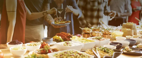 A catering buffet table filled with various dishes, salads, and bowls, with people serving themselves.
