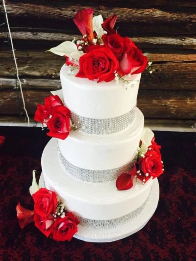 A three-tiered white wedding cake adorned with red roses and silver bands.