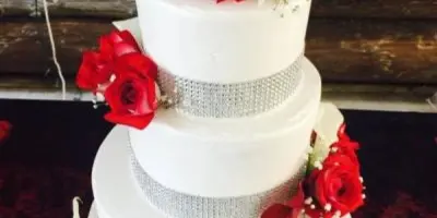 A three-tiered white wedding cake adorned with red roses and silver bands.
