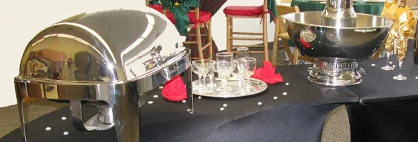 A catering setup featuring a stainless steel chafing dish, a chocolate fountain, and glassware on a table.