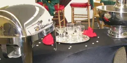 A catering setup featuring a stainless steel chafing dish, a chocolate fountain, and glassware on a table.