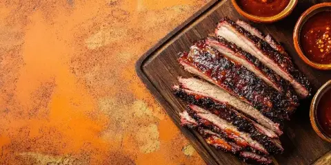 Sliced barbecue brisket on a wooden serving board with small bowls of sauce.