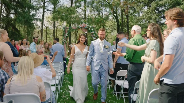 A bride and groom walking down the aisle at an outdoor wedding ceremony while guests throw petals.