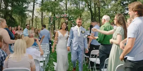 A bride and groom walking down the aisle at an outdoor wedding ceremony while guests throw petals.