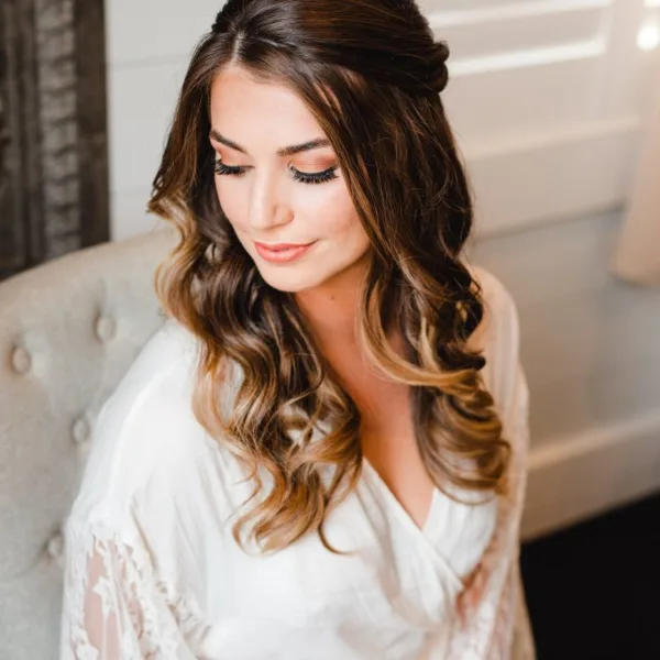 A bride with styled wavy hair and professional makeup wearing a white robe.