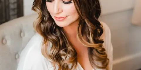 A bride with styled wavy hair and professional makeup wearing a white robe.