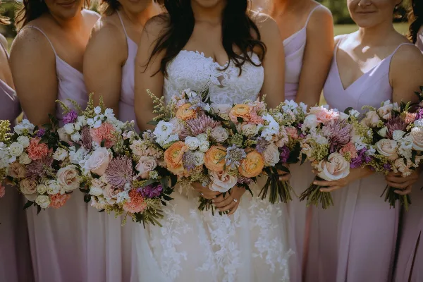 Bride and bridesmaids holding colorful wedding bouquets with roses and dahlias