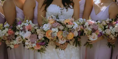 Bride and bridesmaids holding colorful wedding bouquets with roses and dahlias