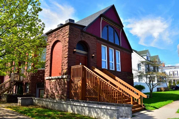 Exterior view of a historic red brick and stone building with a wooden staircase and arched windows.