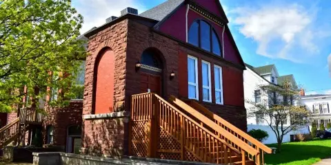 Exterior view of a historic red brick and stone building with a wooden staircase and arched windows.