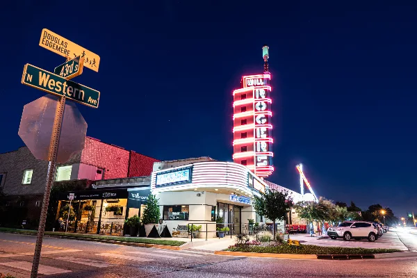 Nighttime exterior view of the Will Rogers Theatre building with its illuminated neon tower and marquee.