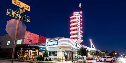 Nighttime exterior view of the Will Rogers Theatre building with its illuminated neon tower and marquee.
