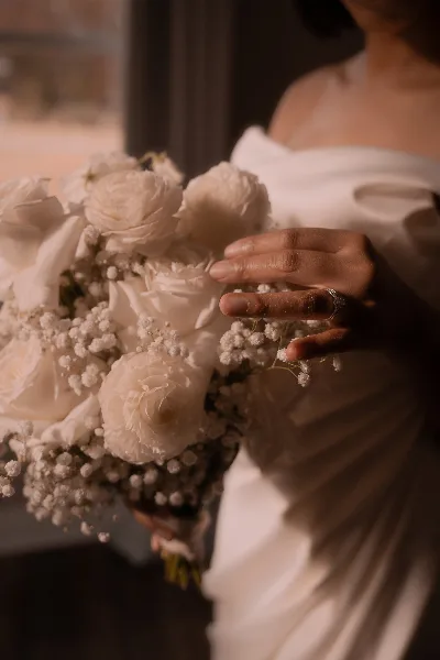 A bride in a white gown holding a bouquet of white roses and baby's breath.