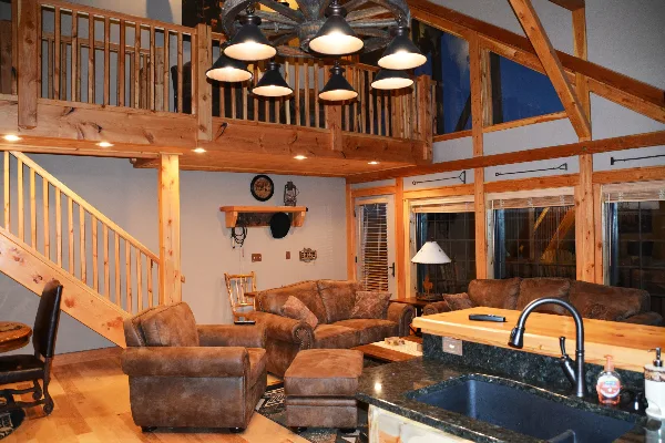 Interior view of a rustic lodge featuring exposed wooden beams, a loft area, leather seating, and a kitchen island.