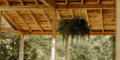 Wedding reception setup with white tables and chairs under a wooden pavilion ceiling with hanging greenery