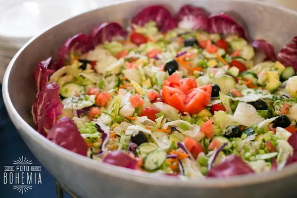 A large catering bowl filled with a fresh salad containing lettuce, tomatoes, cucumbers, and olives.