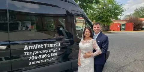 A bride and groom posing next to a black AmVet Transit van in a parking lot.