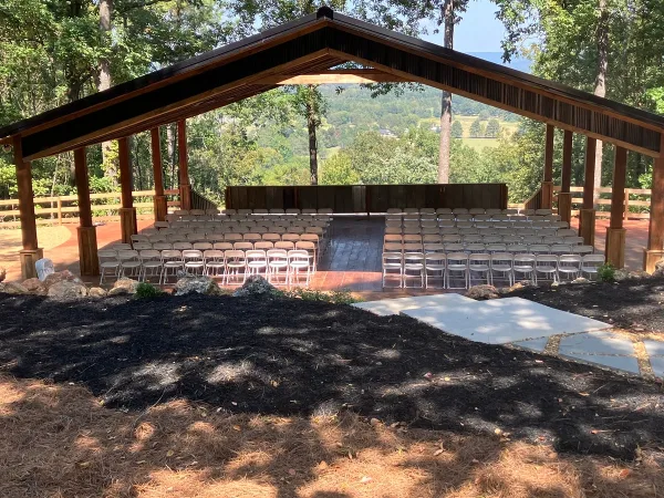 An open-air wooden wedding pavilion with rows of white chairs set up for a ceremony, overlooking a scenic valley view.