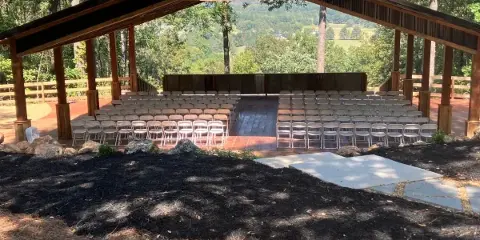 An open-air wooden wedding pavilion with rows of white chairs set up for a ceremony, overlooking a scenic valley view.