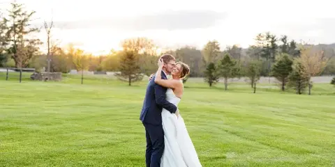 A bride and groom embracing on a green lawn during a wedding photoshoot.