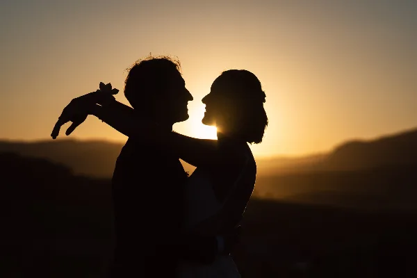 Silhouette of a bride and groom embracing against a sunset mountain backdrop.