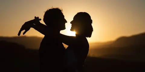 Silhouette of a bride and groom embracing against a sunset mountain backdrop.