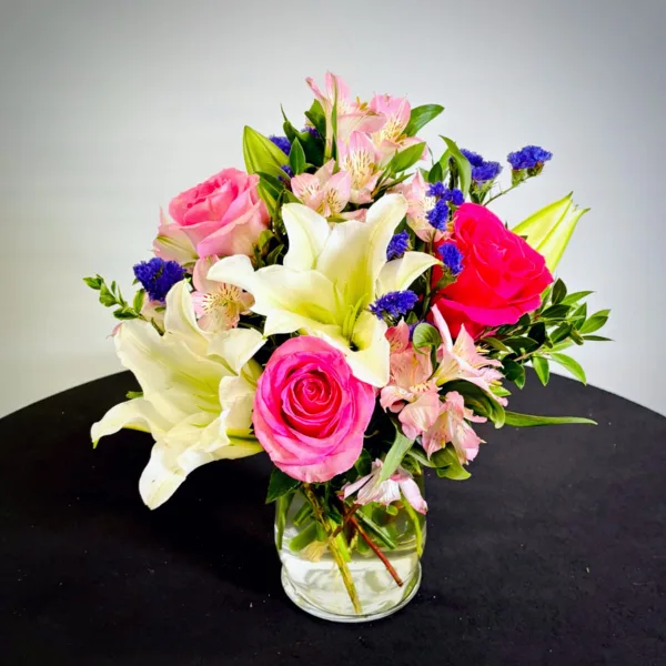 A floral arrangement with pink roses, white lilies, and pink alstroemeria in a clear glass vase.