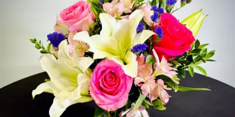 A floral arrangement with pink roses, white lilies, and pink alstroemeria in a clear glass vase.