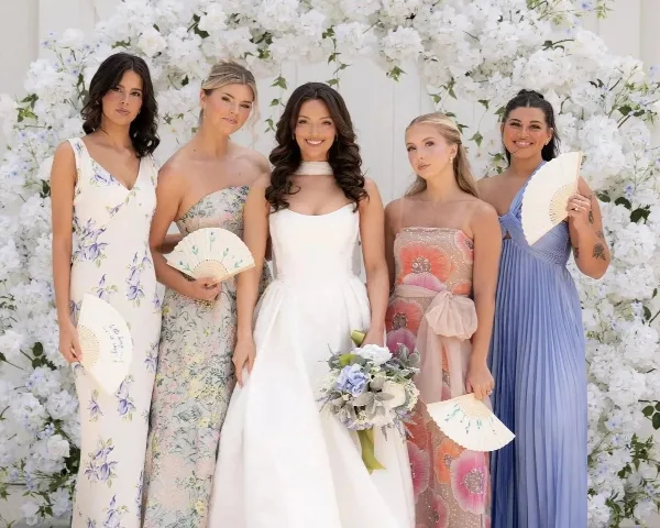 A bride and four bridesmaids posing in front of a white floral wall backdrop.