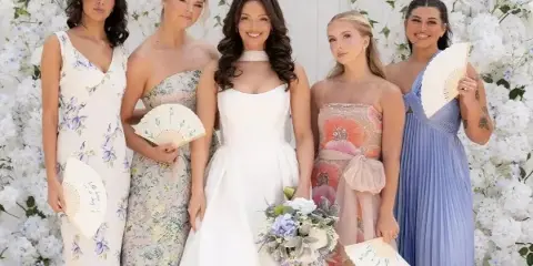 A bride and four bridesmaids posing in front of a white floral wall backdrop.